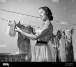 1950s-smiling-woman-housewife-hanging-wash-on-clothesline-to-dry-AAKRBT